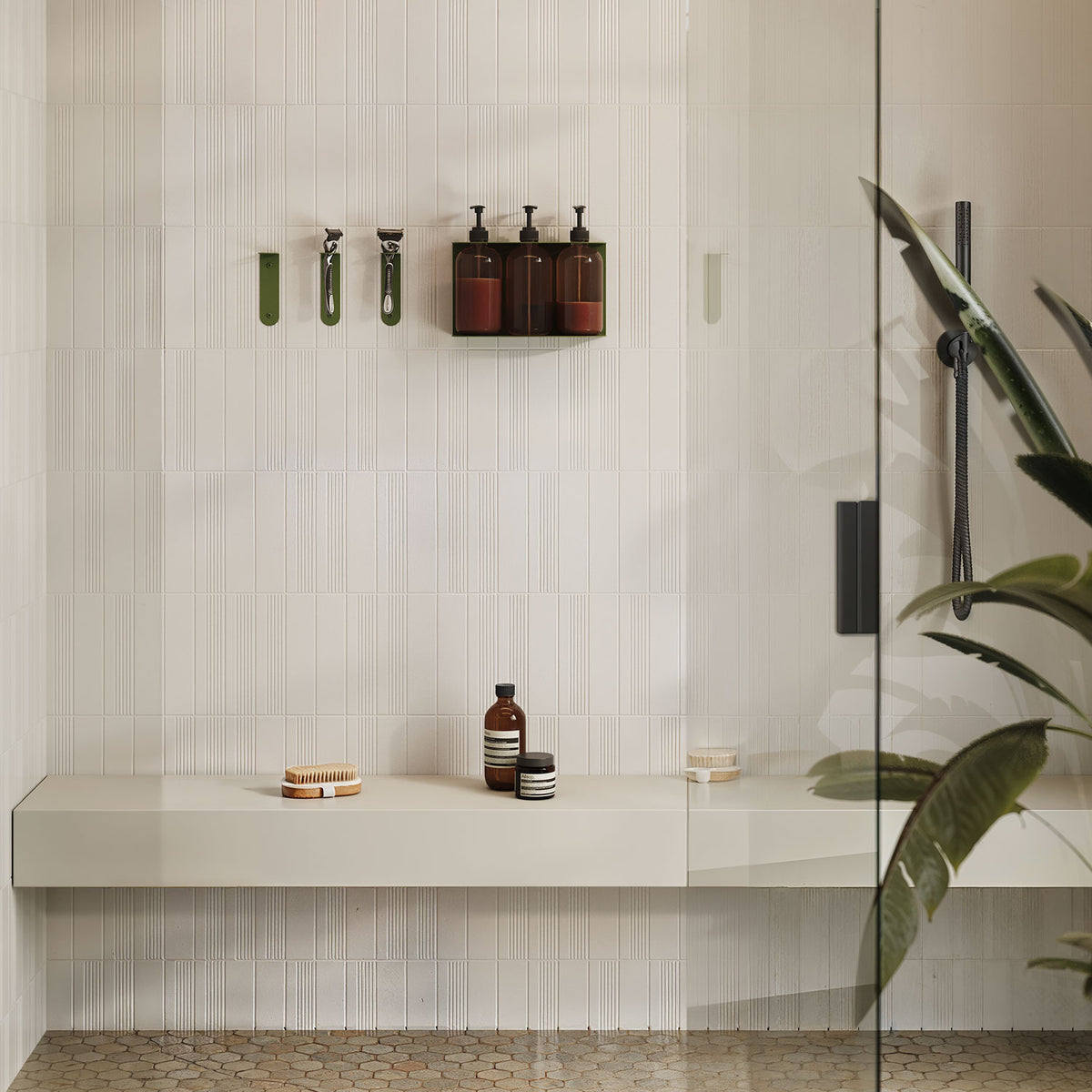 Soap Opera Shower Dispenser mounted on a white tiled shower wall with dark bottles, minimalist green hooks, and a beige floating bench below.