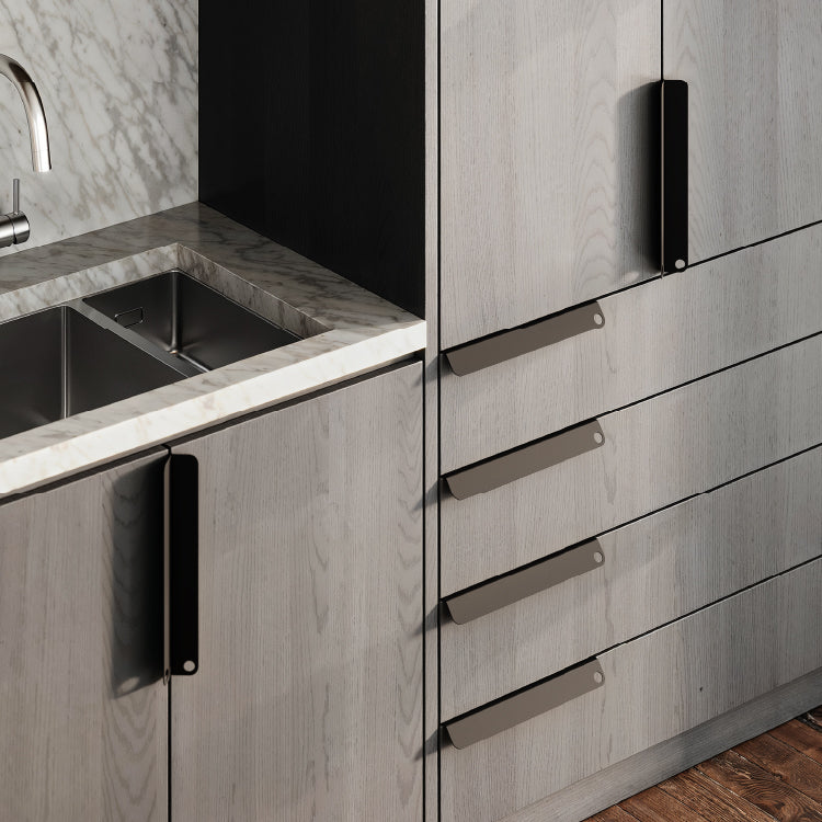 Gray oak cabinetry with large black metal pulls next to a stainless steel dual basin sink under marble counters