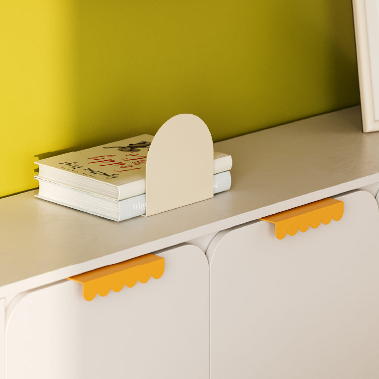 Light beige bookend holding two books on a white cabinet with scalloped orange drawer pulls against a green wall