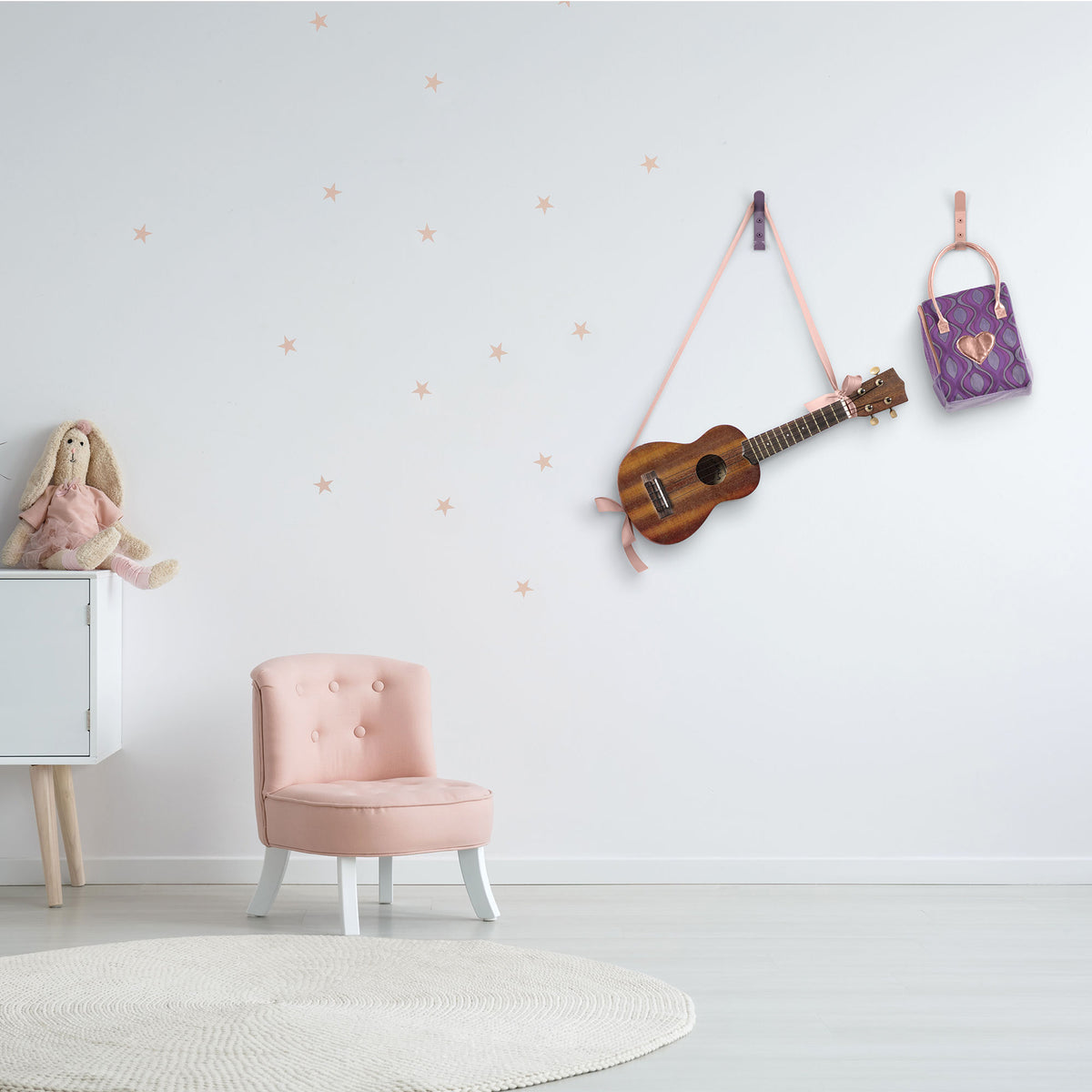 Pink chair beneath a wall mounted ukulele and handbag with a doll seated on a white cabinet and star decals on the wall