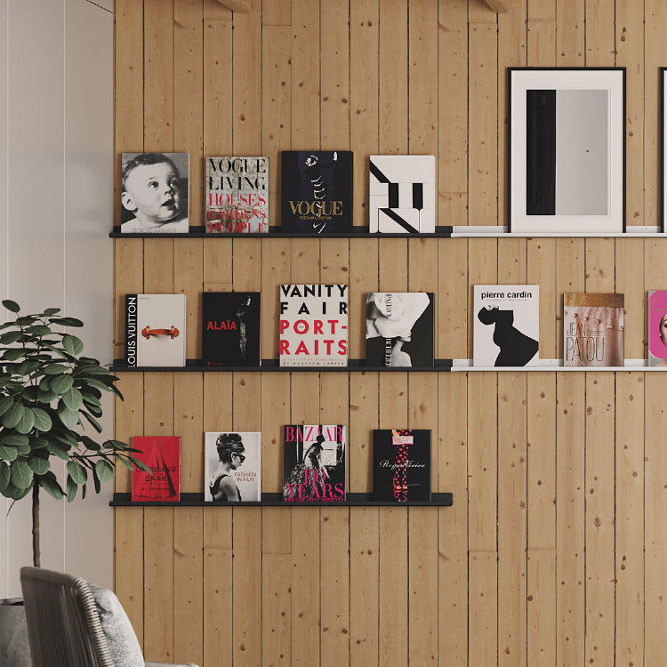 Three rows of slim black and white floating picture rails mounted on natural wood plank wall displaying books and framed art