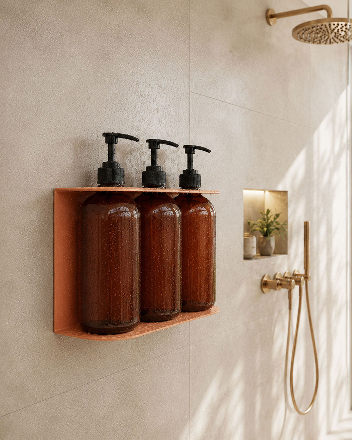 Wall mounted wood shelf holding three amber soap dispensers in a tiled shower with brass fixtures and natural light