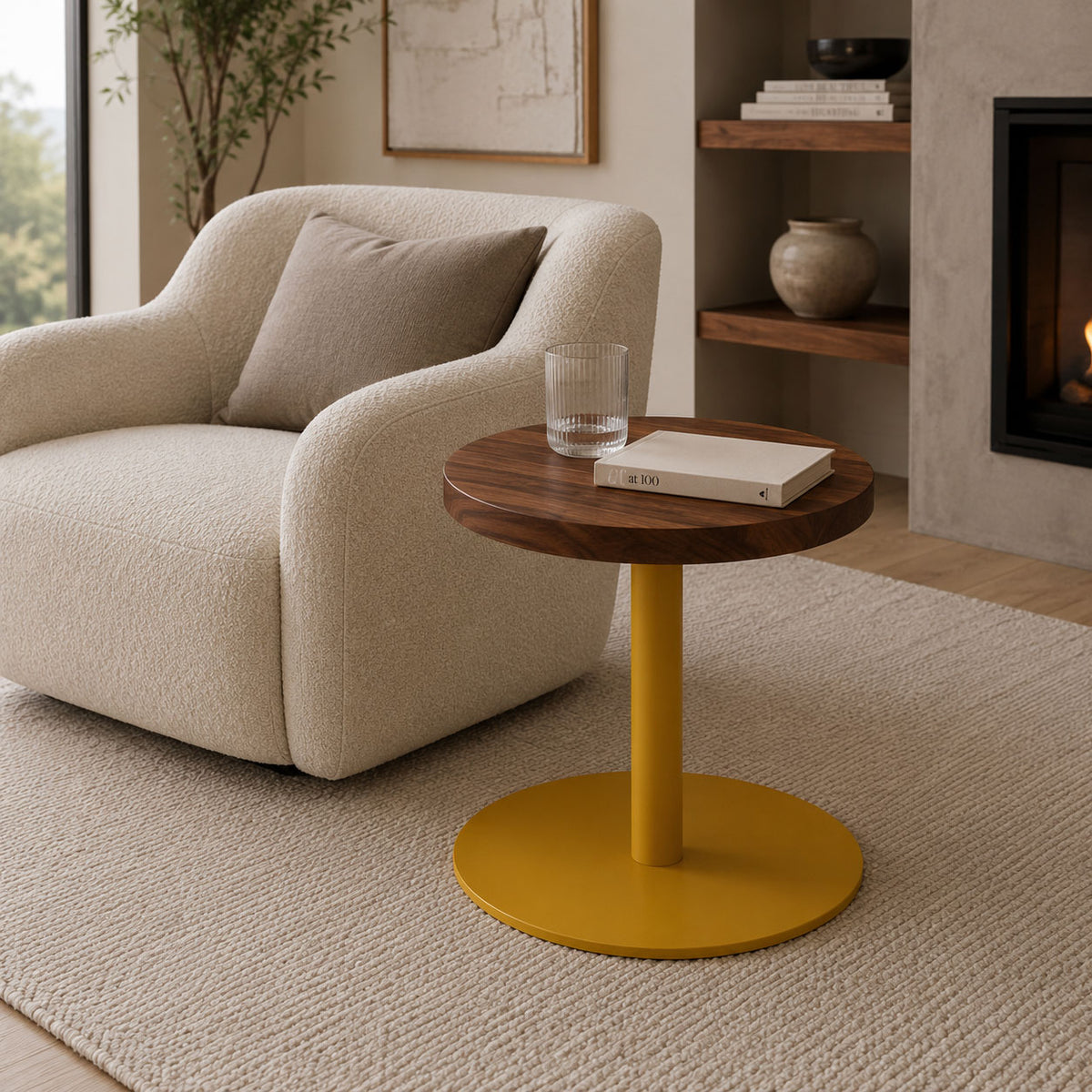 Living room with a cream armchair and round wood-top side table holding a glass and books beside built-in shelves and a lit fireplace