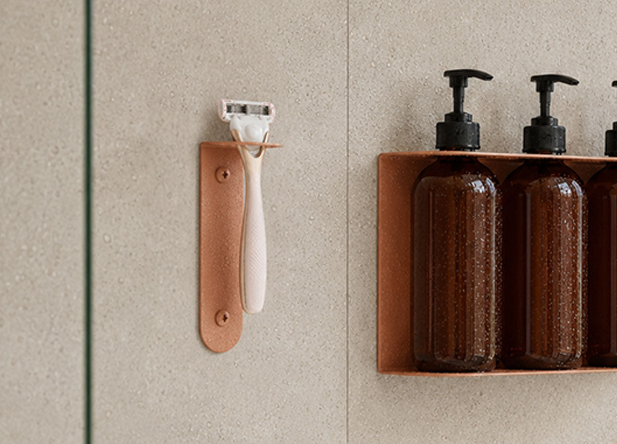 Bathroom wall with a leather razor holder and a wall shelf holding amber pump bottles