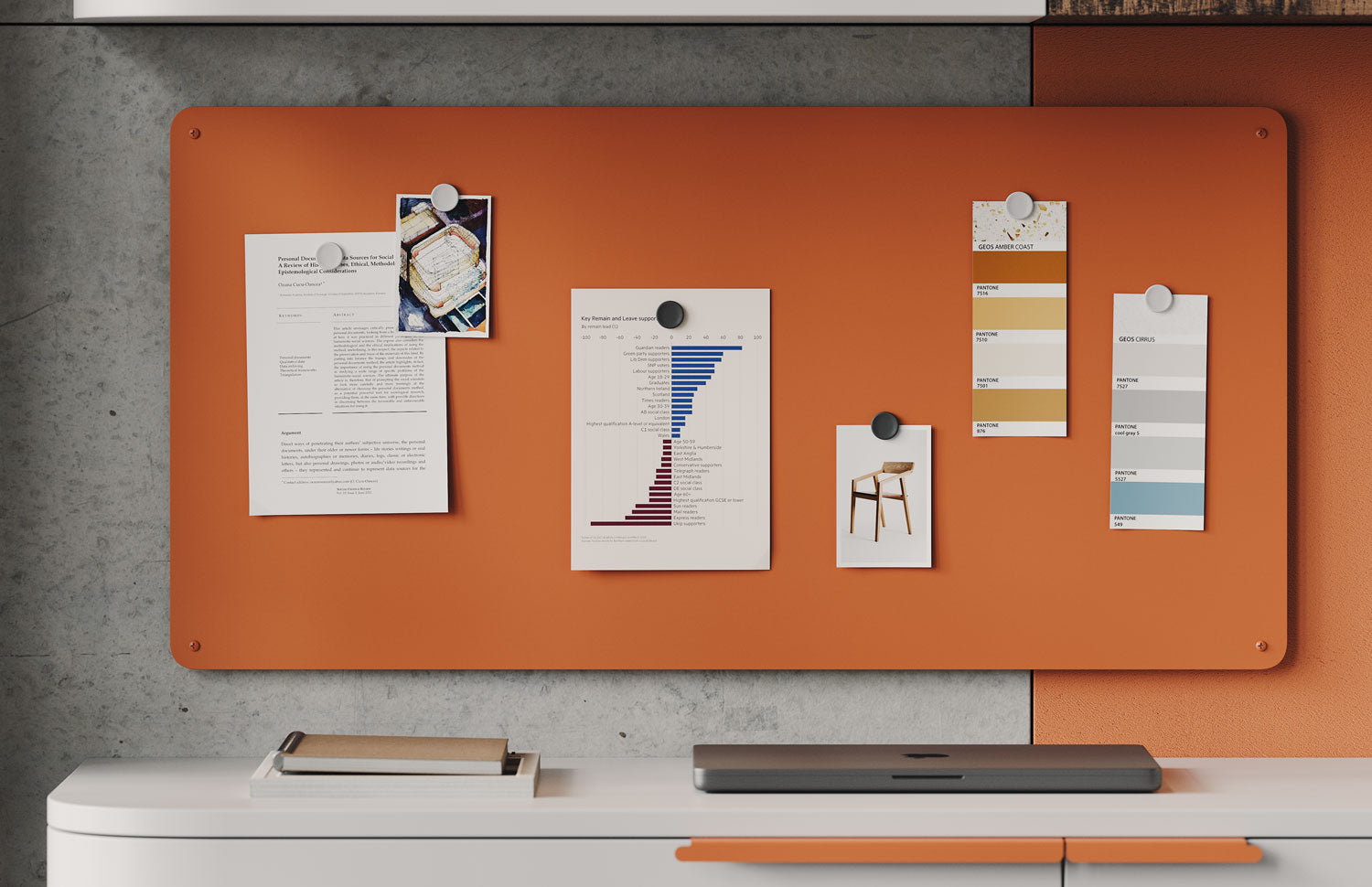 Orange wall-mounted magnetic board with pinned papers, charts, and color swatches above a white cabinet with a closed laptop and notebook.