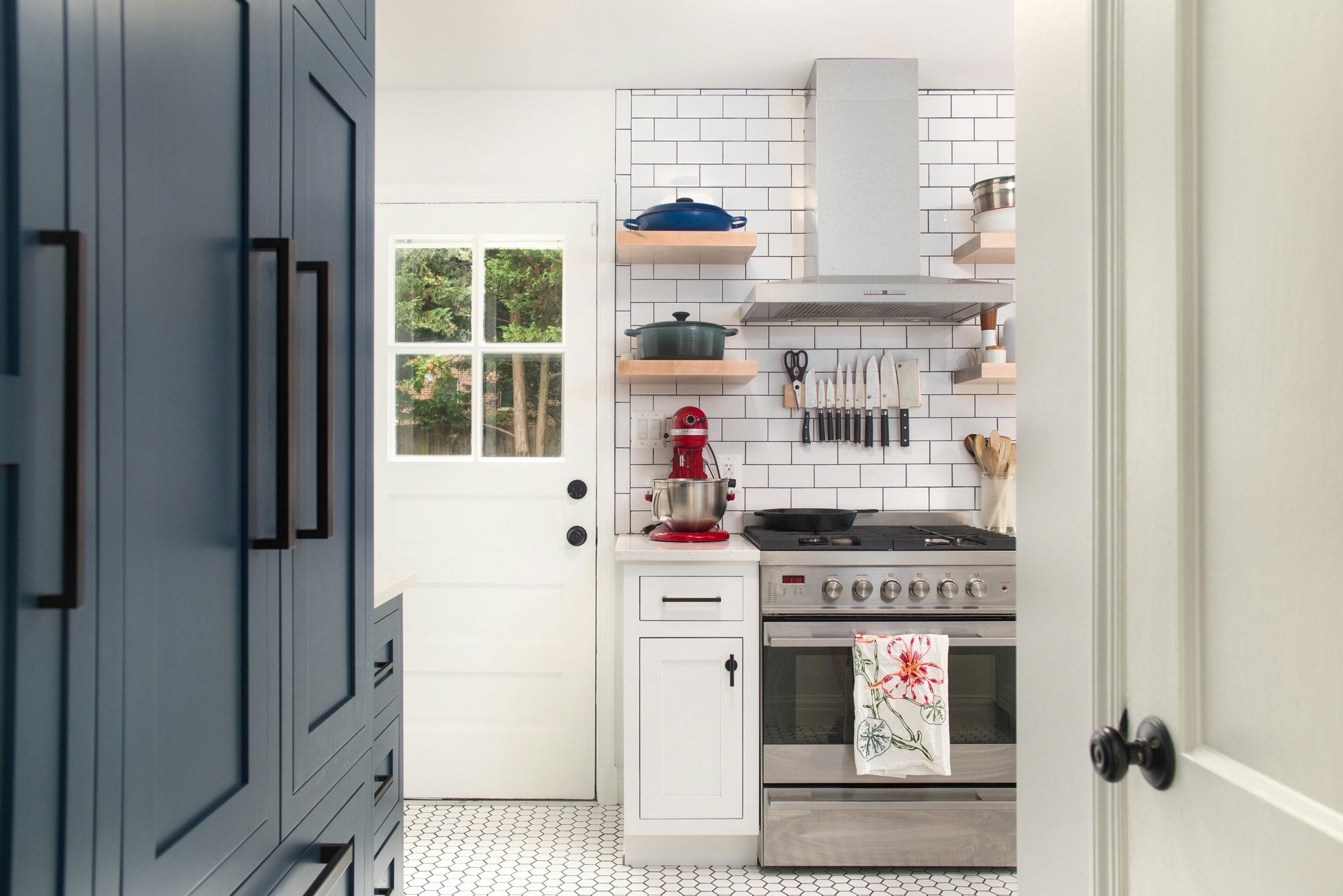 Modern kitchen with Aksel wood floating shelves flanking a range hood, styled with cookware and utensils against a white subway tile backsplash.