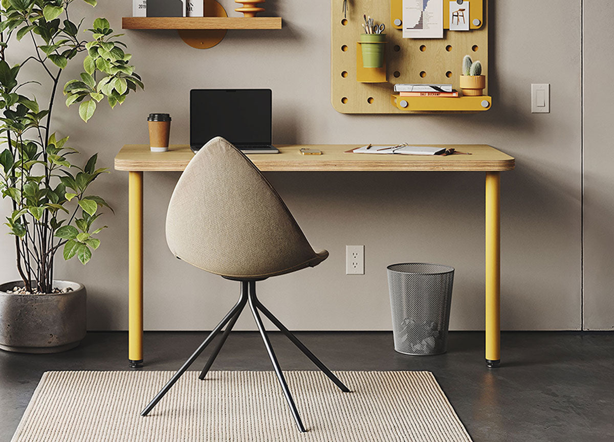 Minimalist home office with a wooden desk, upholstered chair, wall pegboard, wooden shelf, potted plant, and wastebasket