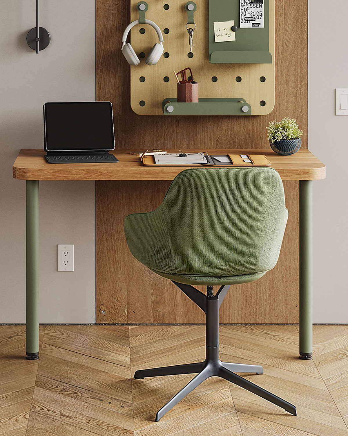 Home workspace with a wood desk, green chair, laptop, and wall-mounted pegboard holding headphones and small accessories