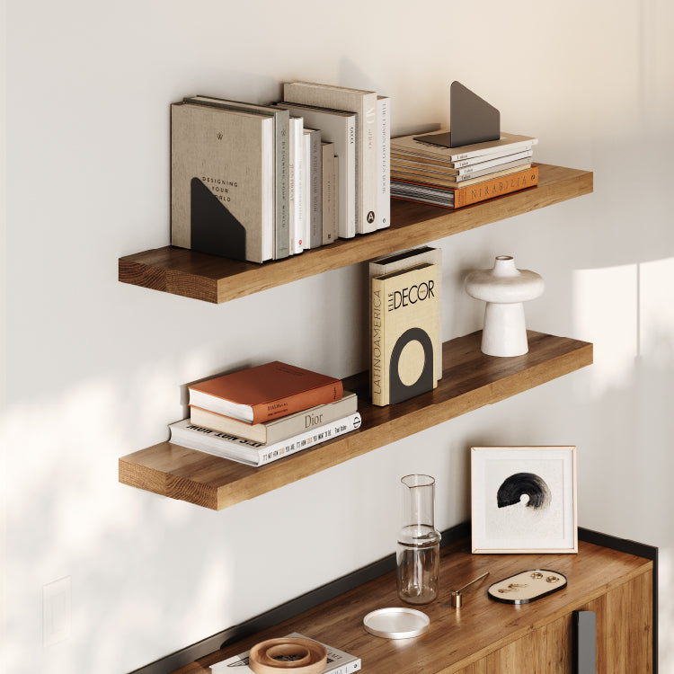 Two wood floating shelves mounted on a light wall displaying books held by minimalist matte black metal bookends and decor pieces.