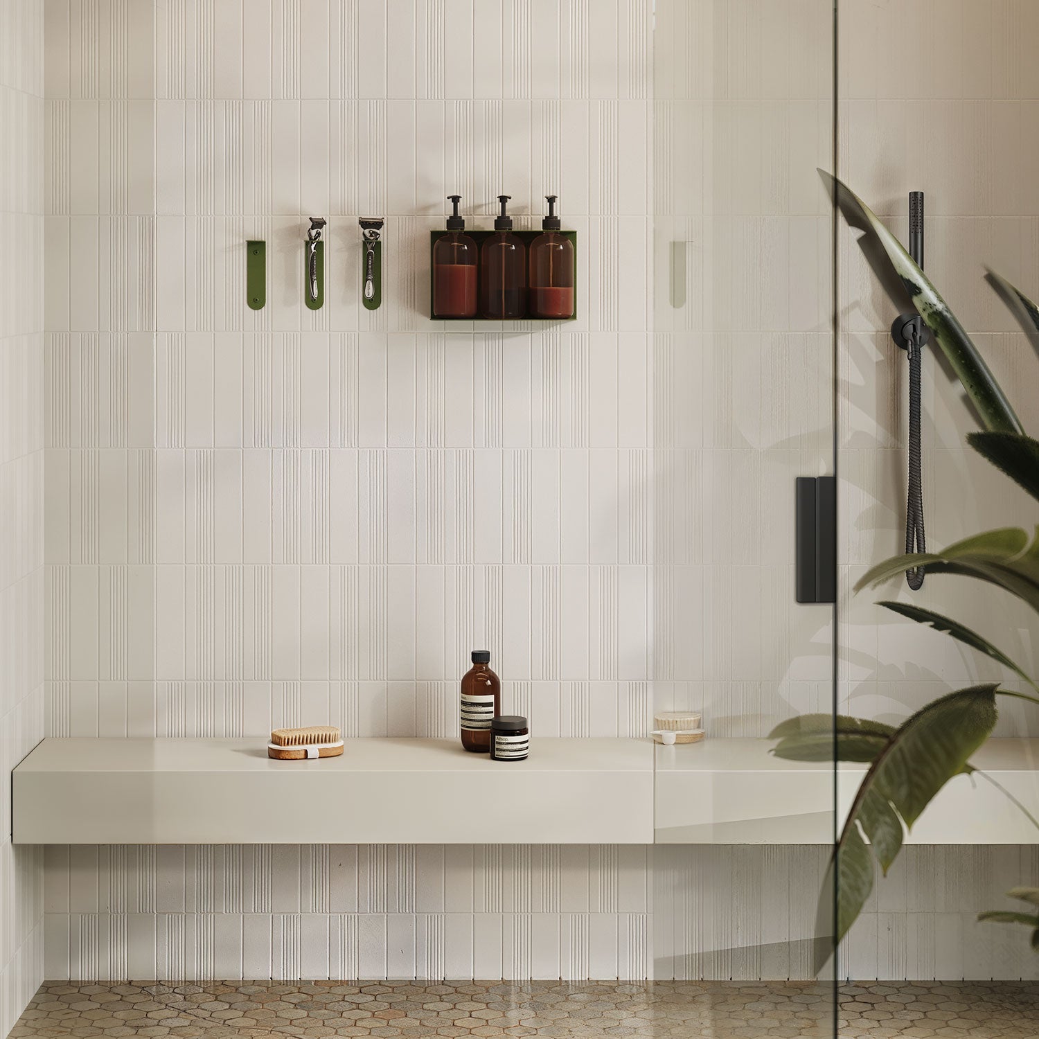 Soap Opera Shower Dispenser mounted on a white tiled shower wall with dark bottles, minimalist green hooks, and a beige floating bench below.