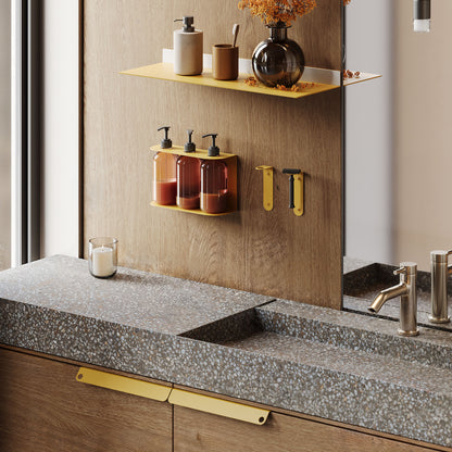 Soap Opera Shower Dispenser with three amber bottles mounted on a wall above a terrazzo countertop near a modern brass shelf holding bathroom decor.