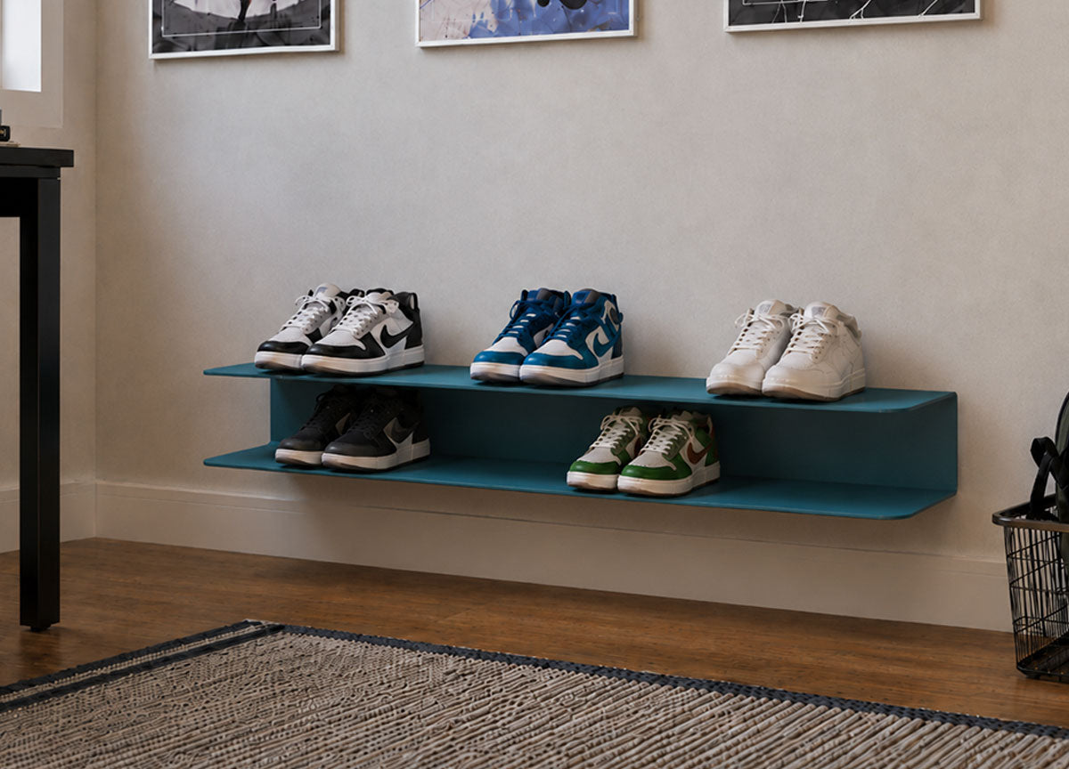 Minimalist floating wall shelf in blue holding six pairs of sneakers, installed in a modern room with hardwood floors and framed artwork above.