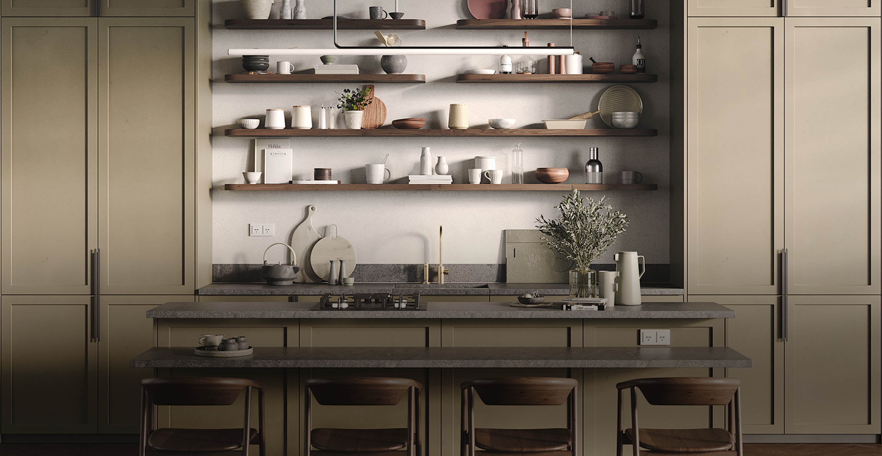 Muted olive kitchen cabinetry framing wood floating shelves with ceramics and greenery above a stone countertop island and bar stools.