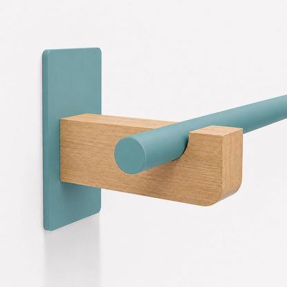 Close-up of a minimalist Draper Curtain Rod System bracket featuring a solid hardwood block and teal metal rod against a white wall.