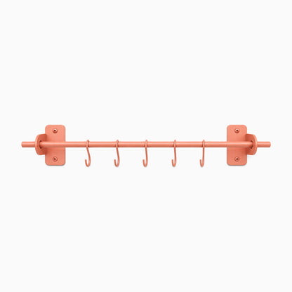 Etta Utensil Rack in matte coral finish with wall mounts and six hooks, a minimalist, durable metal wall shelf bracket for organizing utensils.