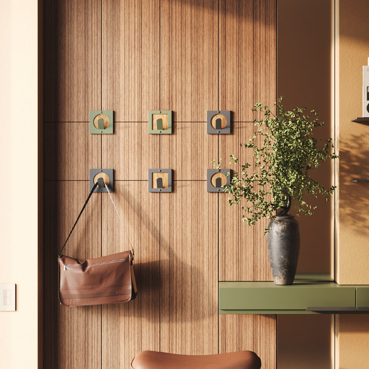 Square wall hooks with circular wooden accents mounted on vertical wood paneling holding a leather bag next to a green drawer and vase