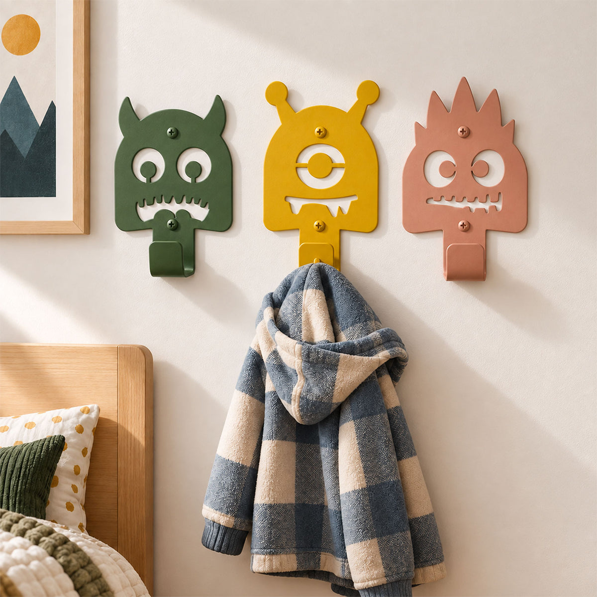 Little Hangups colorful monster wall hooks holding a child’s plaid jacket beside a bed