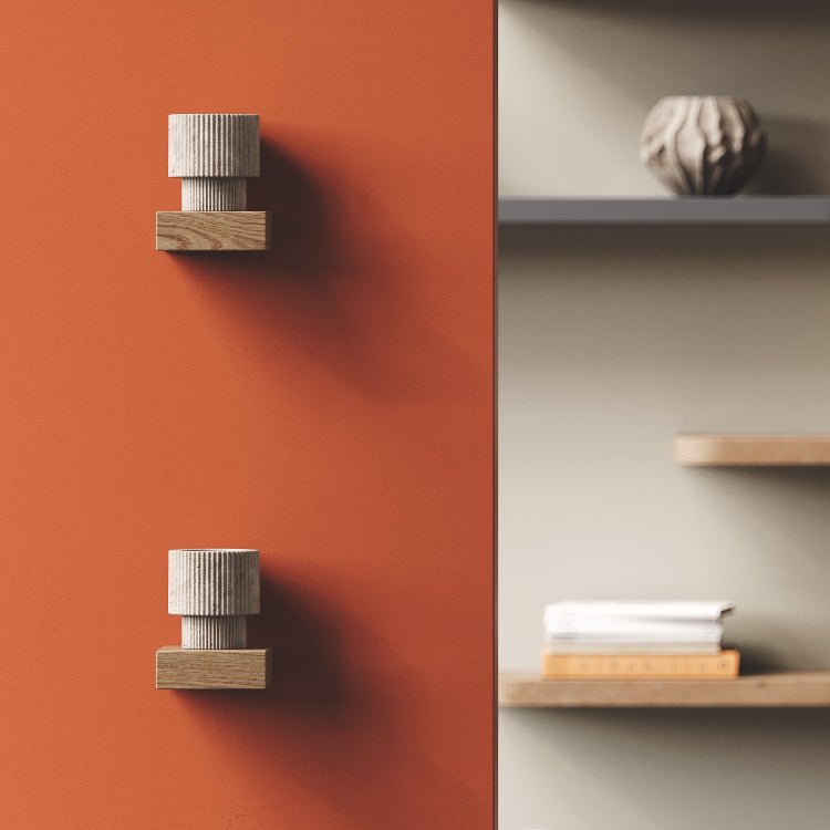 Two small wood and ribbed ceramic wall hooks mounted on a warm rust-colored wall next to light wood floating shelves with decor.