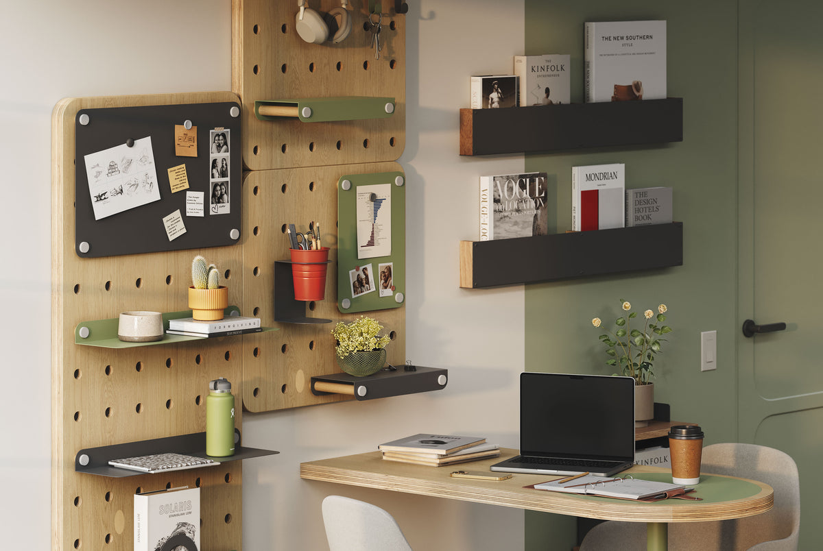 Organized home office with a wood pegboard, black wall shelves, desk, computer monitor, and assorted notes and decor.