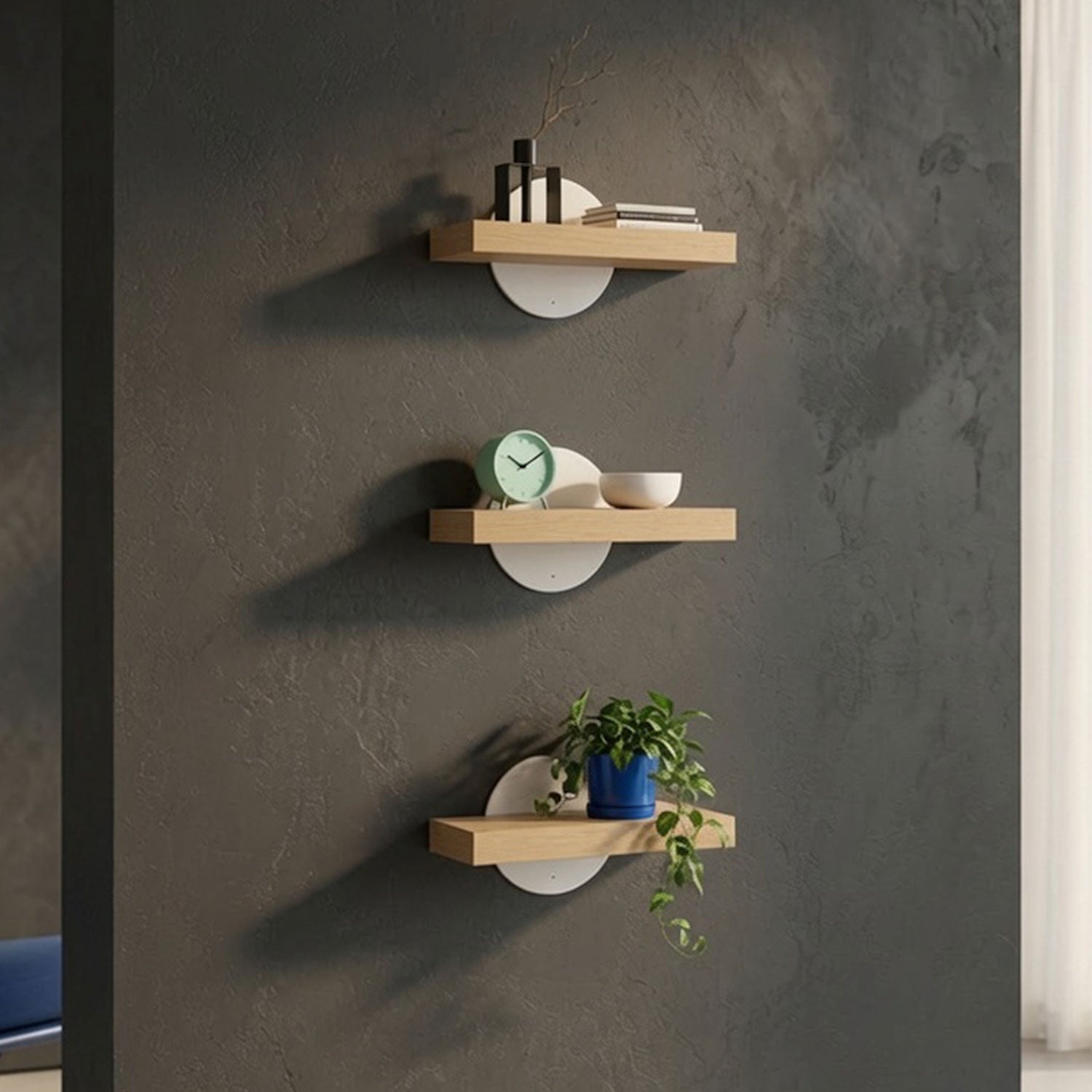 Three Shortie Deux Wall Shelves mounted on a dark textured wall displaying decorative items including books, a clock, a bowl, and a potted plant in a minimalist, functional design that maximizes wall space.