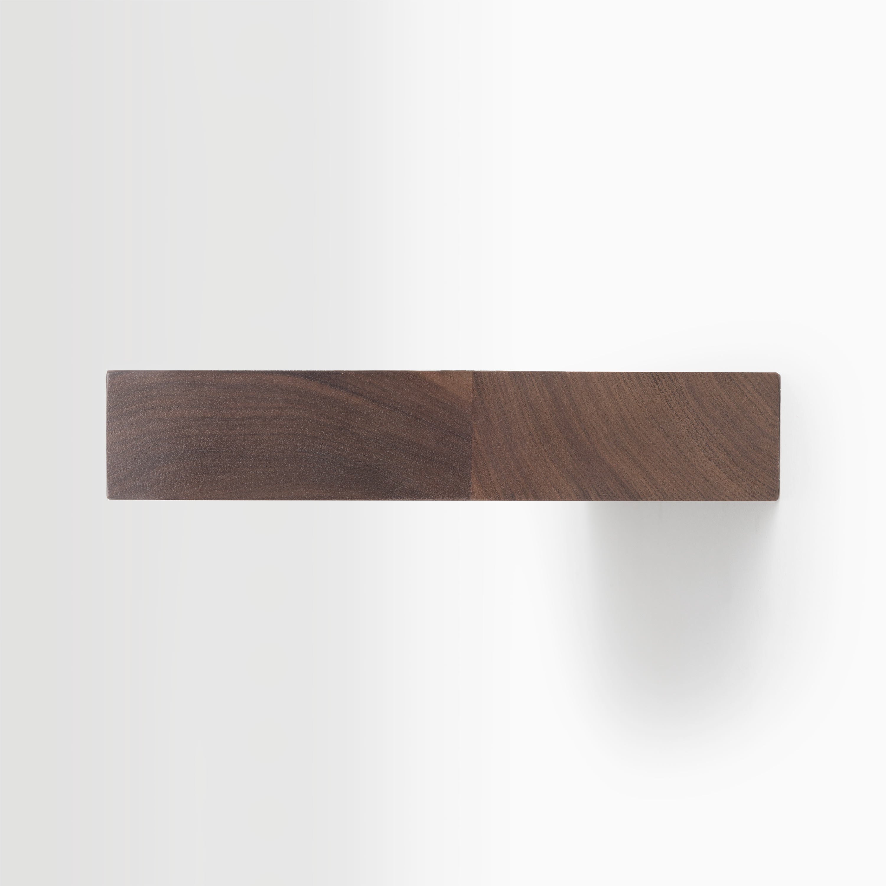 Top view of a solid walnut wood block with smooth finish casting a subtle shadow on a white background
