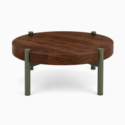 Stay Coffee Table featuring a round solid hardwood top with matte olive green metal legs, combining minimalist design and durable craftsmanship.