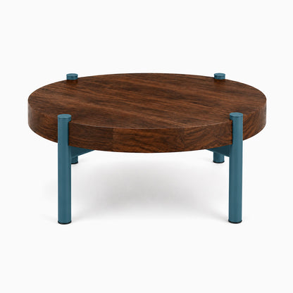 Stay Coffee Table featuring a round solid hardwood top with a rich walnut finish, supported by durable steel legs in a muted blue tone.
