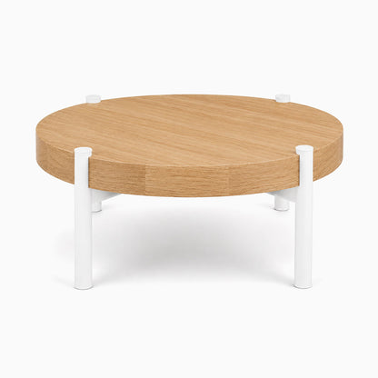 Stay Coffee Table with a round solid hardwood top and minimalist white metal legs, designed for functional and stylish living spaces.